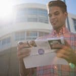 Bright young man reading direct mail envelope in urban setting for direct marketing.