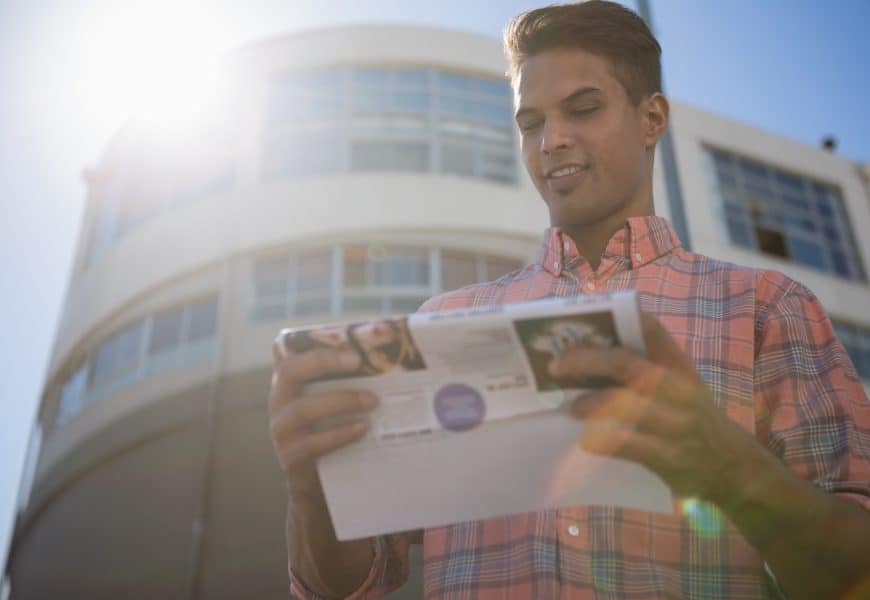 Bright young man reading direct mail envelope in urban setting for direct marketing.