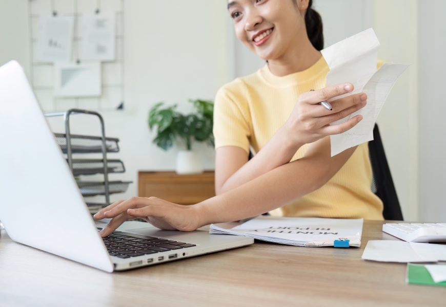 High school woman doing paperwork at desk with laptop.