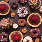 Colorful assortment of decorated cookies and cupcakes on dark surface.