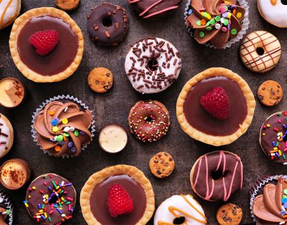 Colorful assortment of decorated cookies and cupcakes on dark surface.