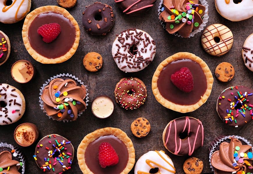 Colorful assortment of decorated cookies and cupcakes on dark surface.