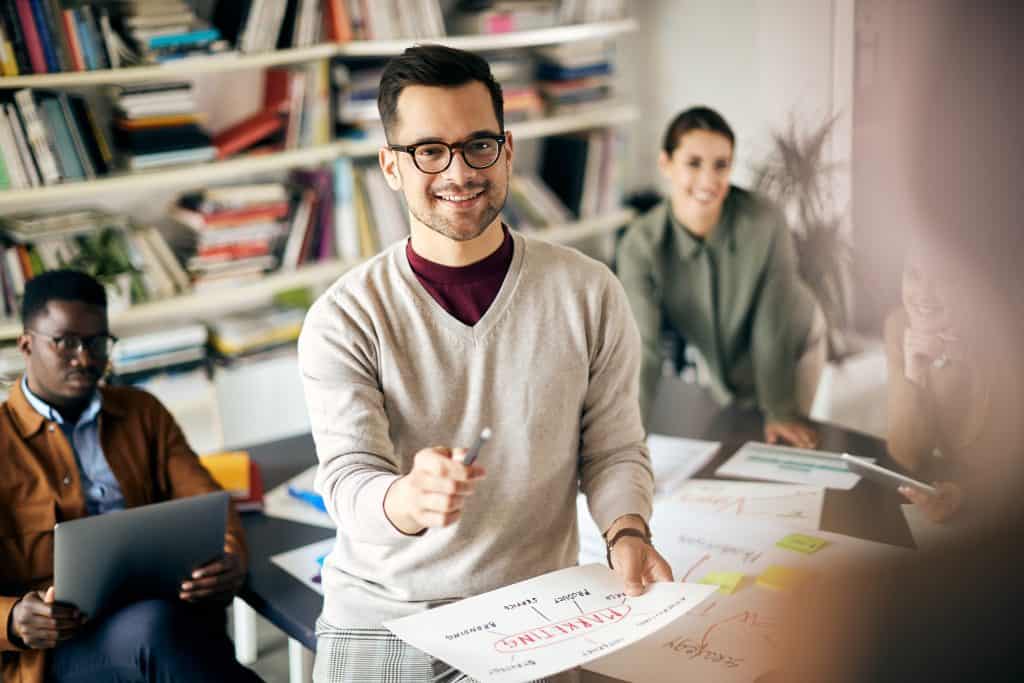 Bright young professional smiling in an office meeting with printed marketing materials on the table.