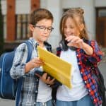 Bright young students with backpacks looking at a tablet outside, promoting effective direct mail marketing strategies.