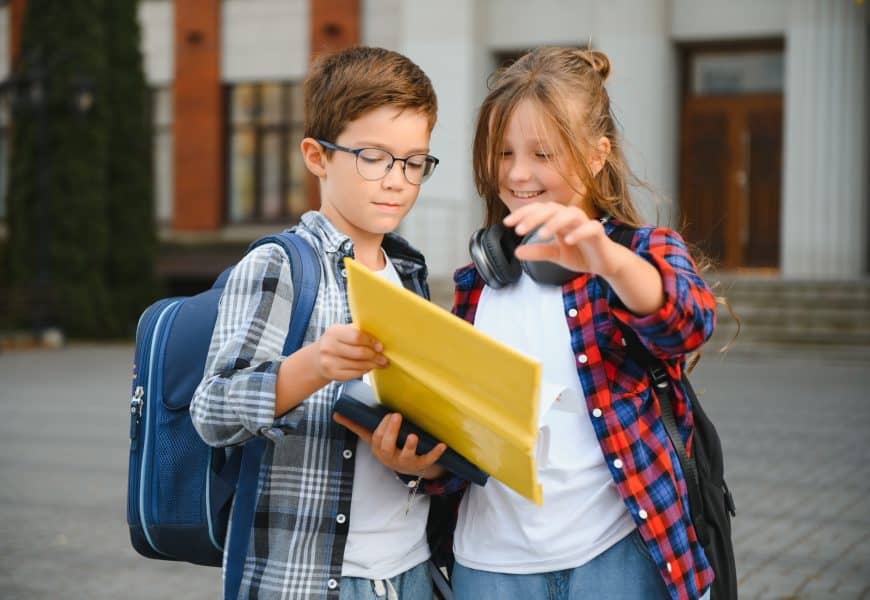 Bright young students with backpacks looking at a tablet outside, promoting effective direct mail marketing strategies.
