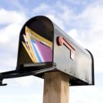 Envelope filled with direct mail marketing materials in a mailbox against a sky background.