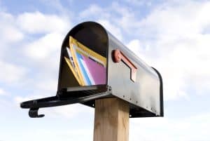 Envelope filled with direct mail marketing materials in a mailbox against a sky background.