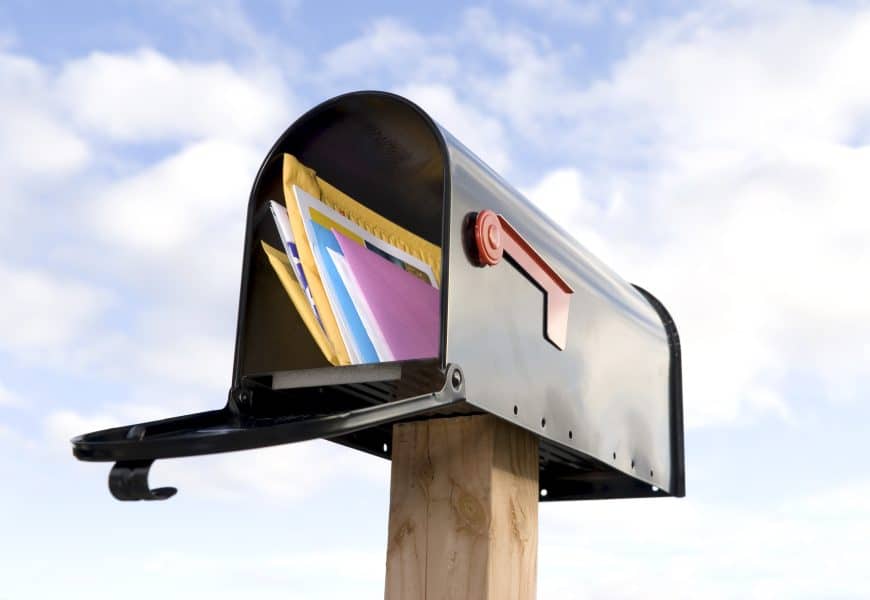 Envelope filled with direct mail marketing materials in a mailbox against a sky background.